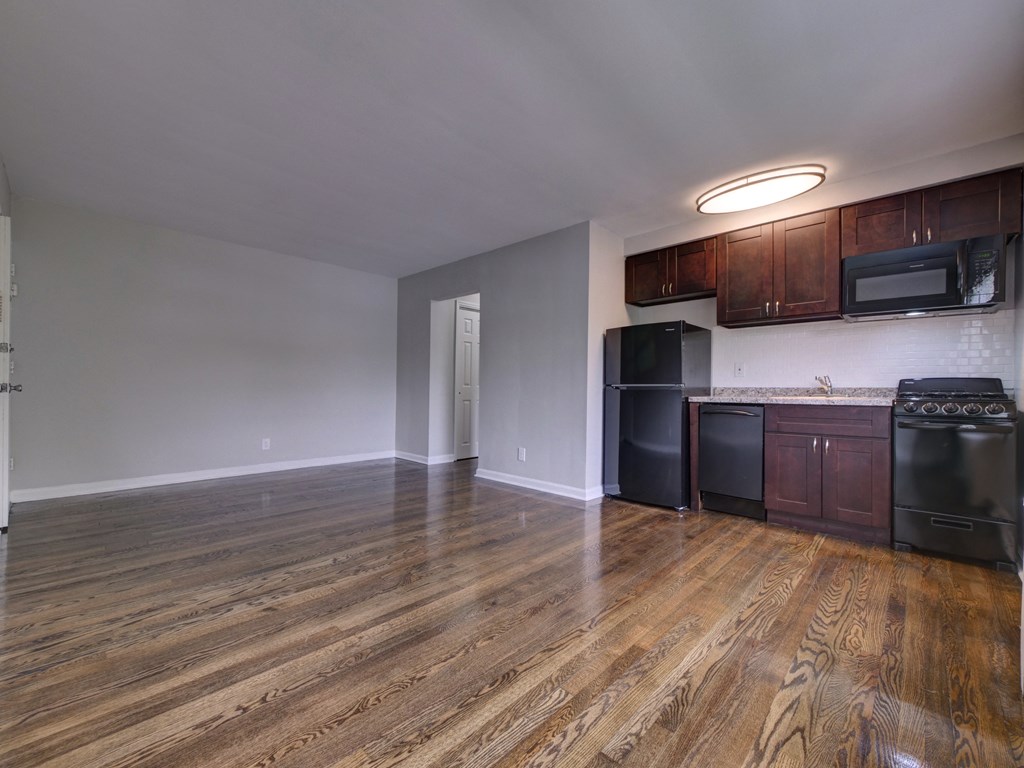 an empty living room with wooden floors and a kitchen with black appliances