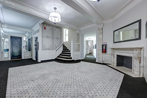 A large white tiled floor in a spacious room with a staircase and a fireplace.
