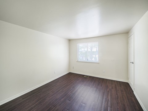 a bedroom with white walls and wood floors and a window