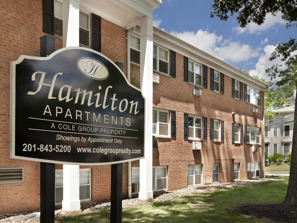 A sign for Hamilton Apartments is in front of a brick building.