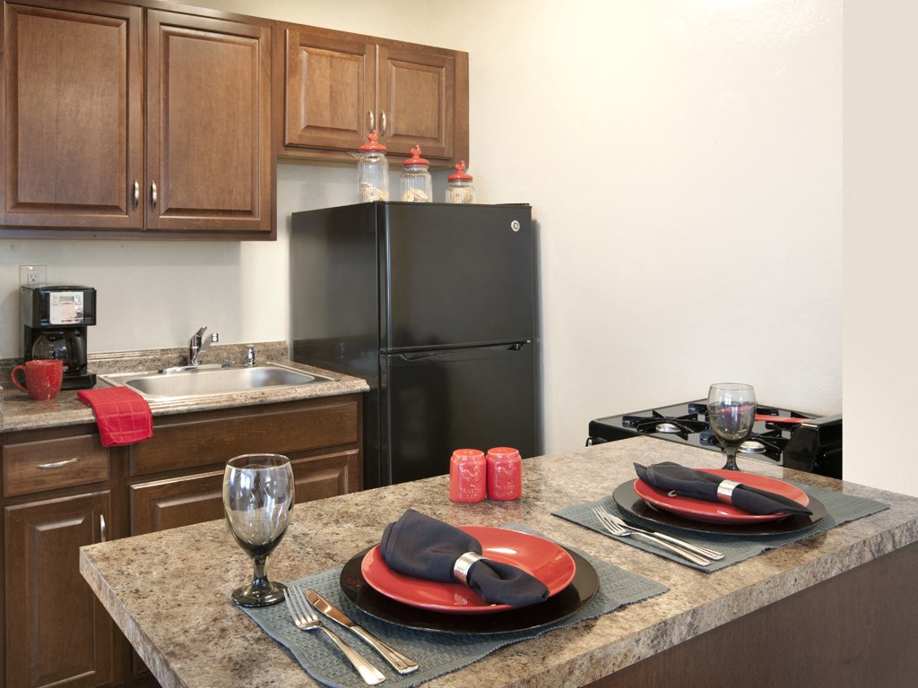 A kitchen with a black refrigerator and a table set for two.