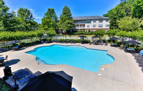 A large swimming pool surrounded by trees and a building in the background.