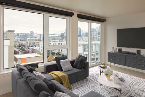 A living room with a grey couch and a large window overlooking a cityscape.