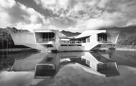 A black and white image of a modern building with a reflective pool in front.