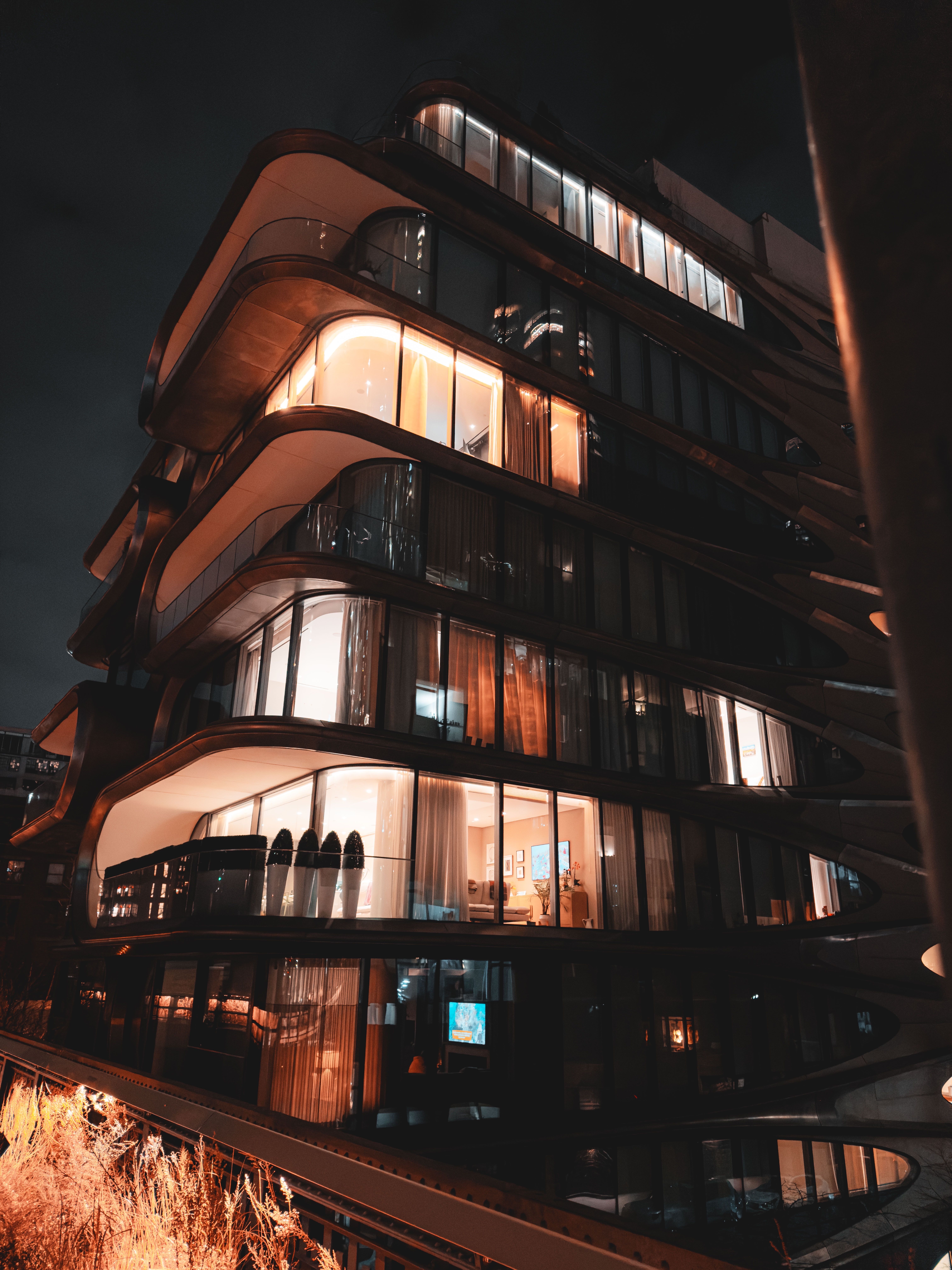 A modern building with curved balconies and lights on inside.