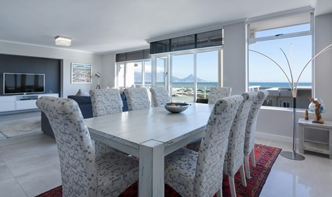 A dining room with a table and chairs with a view of the sea.