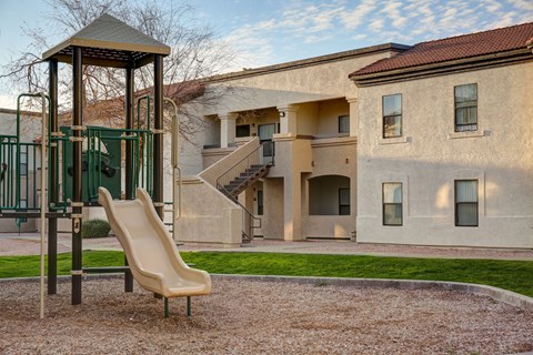 A playground with a slide and a chair in front of a building.