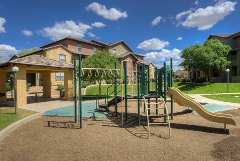 A playground with a slide, swings, and a seesaw in front of a row of houses.