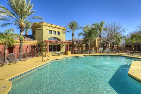 A pool surrounded by palm trees and a building in the background.