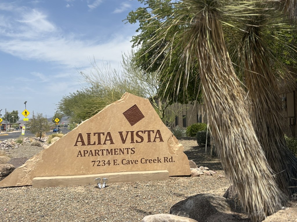 A sign for Alta Vista Apartments stands in front of a palm tree.