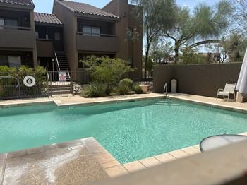 A swimming pool in a backyard with a brown fence and a white chair.