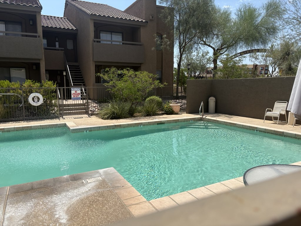 A swimming pool in a backyard with a brown fence and a white chair.