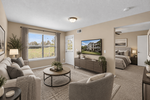 A living room with a grey couch, a coffee table, and a large window with a view of the outside.