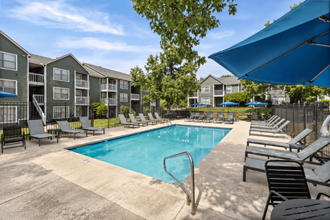 A swimming pool surrounded by lounge chairs and umbrellas in a sunny day.