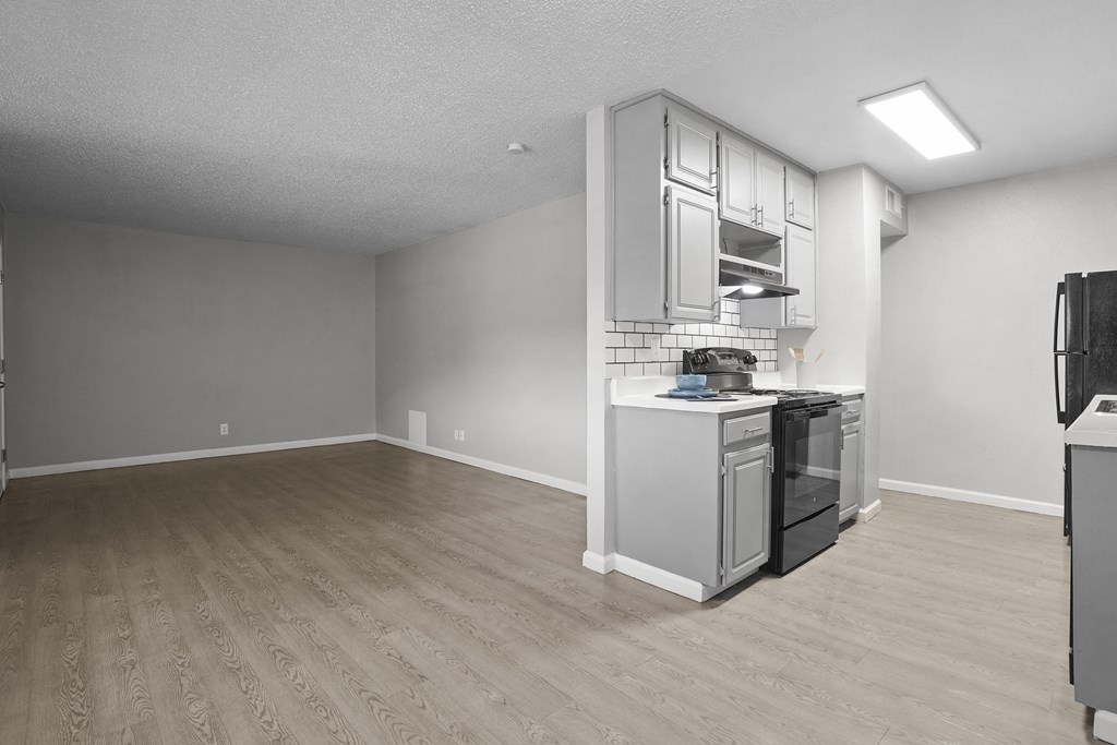 an empty living room with a kitchen with a stove and refrigerator