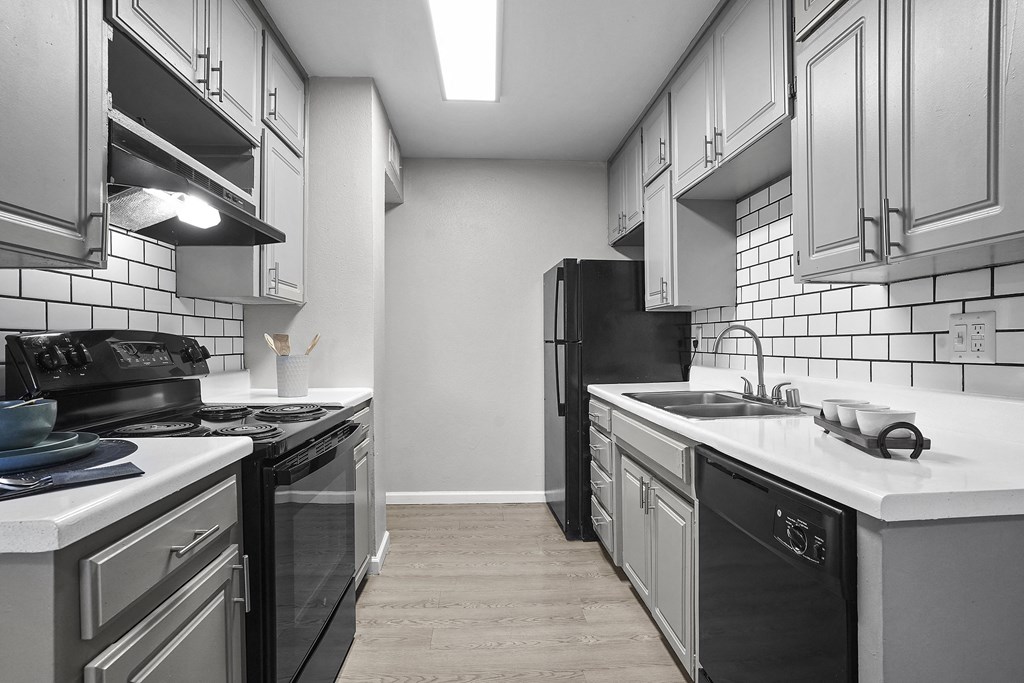 an empty kitchen with white counter tops and black appliances
