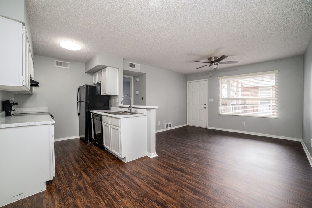 an empty living room with a kitchen and a ceiling fan