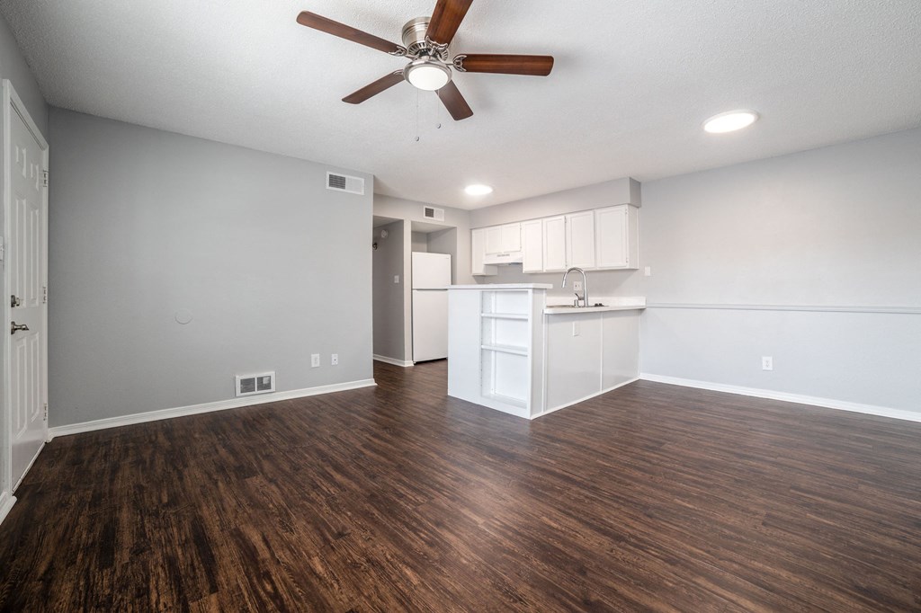 an empty living room and kitchen with a ceiling fan