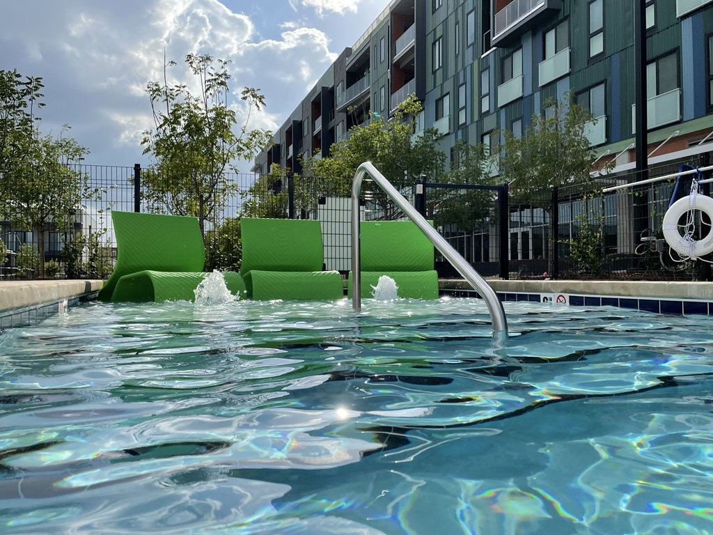 a swimming pool with green chairs in front of a building