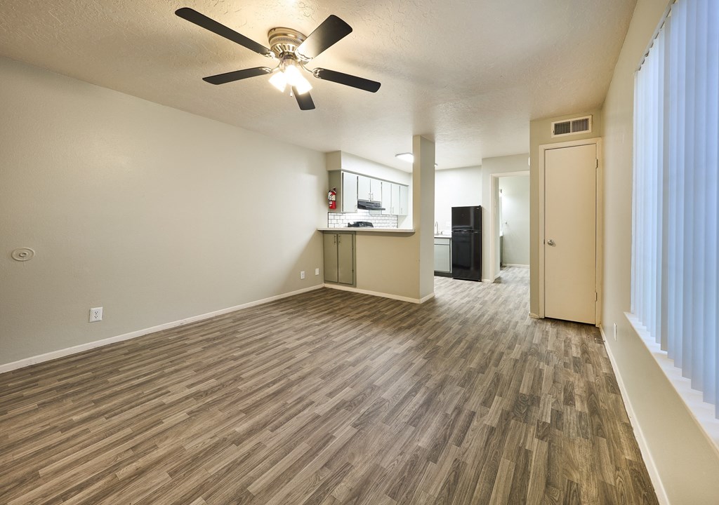 an empty living room with a ceiling fan and a kitchen