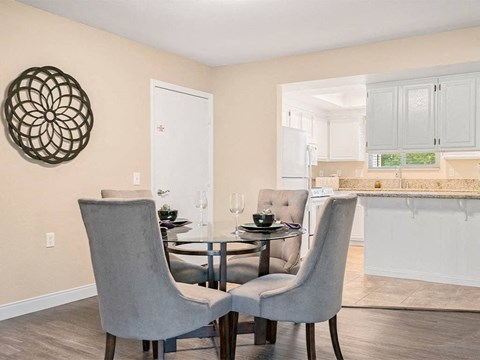 a dining room with a table and chairs and a kitchen in the background