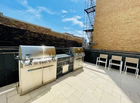 a patio with two barbecue grills and chairs on it