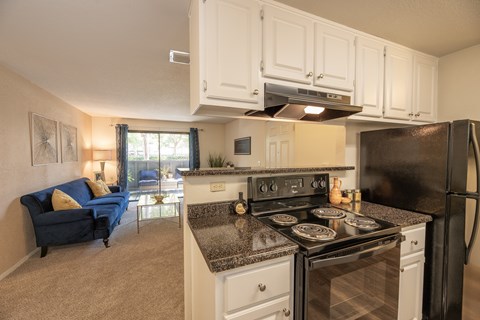 A kitchen with black appliances and a blue couch in the living room.