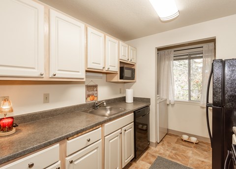 A kitchen with white cabinets and a black fridge.