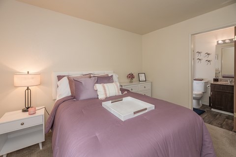 Model primary bedroom with a purple bedspread and a white nightstand with a lamp at Pheasant Pointe Apartments, California, 95833