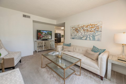A living room with a white couch, a glass coffee table, and a painting on the wall.
