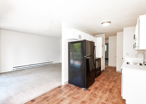 an empty living room with a refrigerator and a kitchen