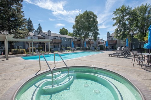 A hot tub sits in the middle of a pool area with a building in the background at Sierra Glen Apartments, California, 95621
