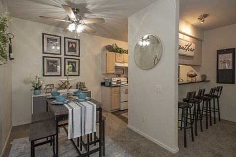 A dining area with a table set for two and a kitchen area with a bar in the background.