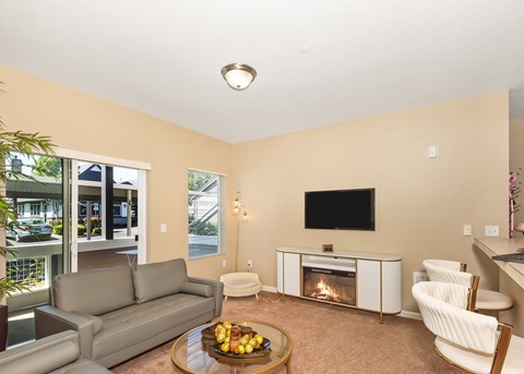 A living room with a grey couch, a coffee table with fruit on it, a fireplace, and a television.