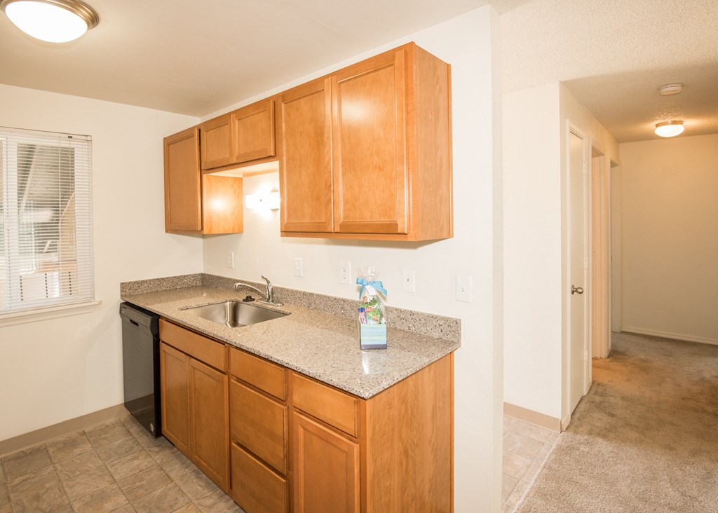 vacant apartment kitchen with stainless steel sink, black dishwasher, and wood cabinets at Todd Village Apartments, Tualatin, Oregon 97062