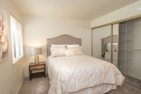 A bedroom with a bed, nightstand, and a mirror at Zinfandel Village Apartments, California, 95670