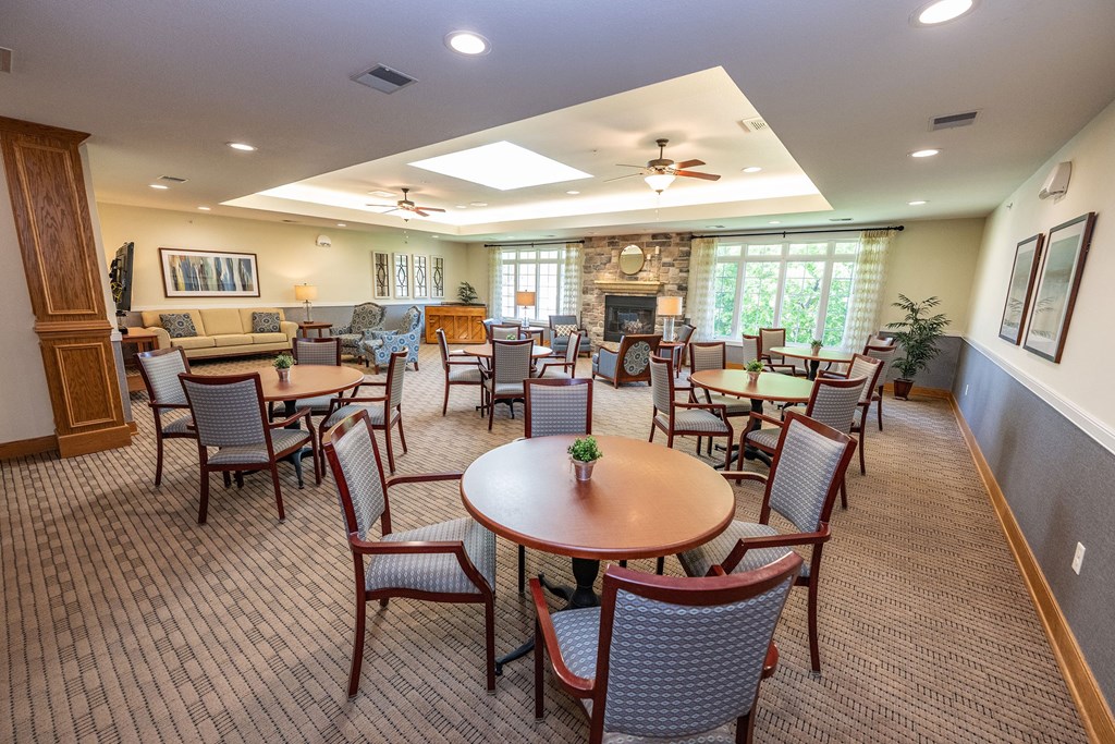 A large room with a table and chairs in the foreground and a fireplace in the background.