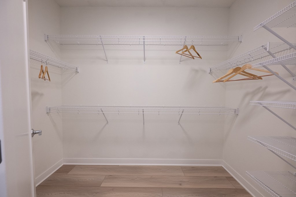 a walk in closet in a home with white walls and shelves and hanging racks