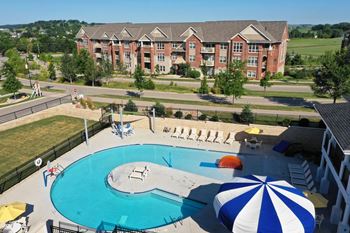 an aerial view of a swimming pool with an umbrella and a building in the background