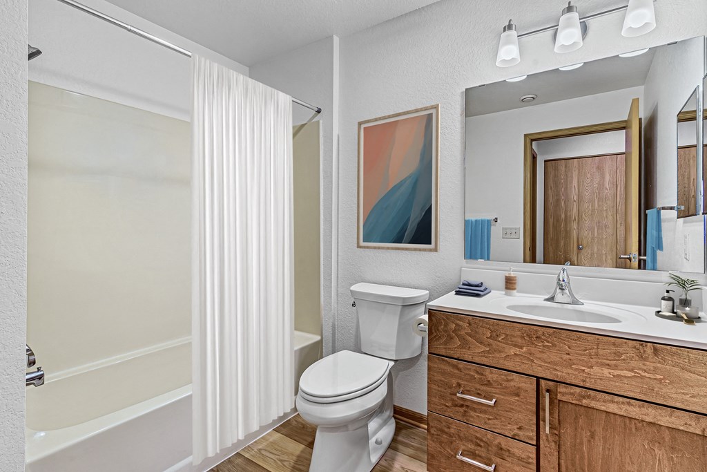 A white toilet sits in a bathroom with a wooden vanity and a mirror.