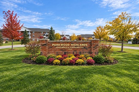A sign for Parkwood Highlands Apartments is surrounded by flowers and trees.