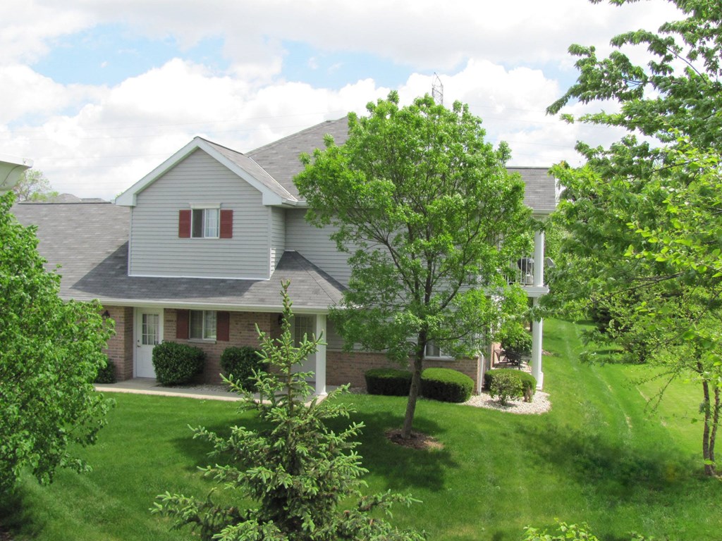 A house with a grey roof and a white door is surrounded by green trees.