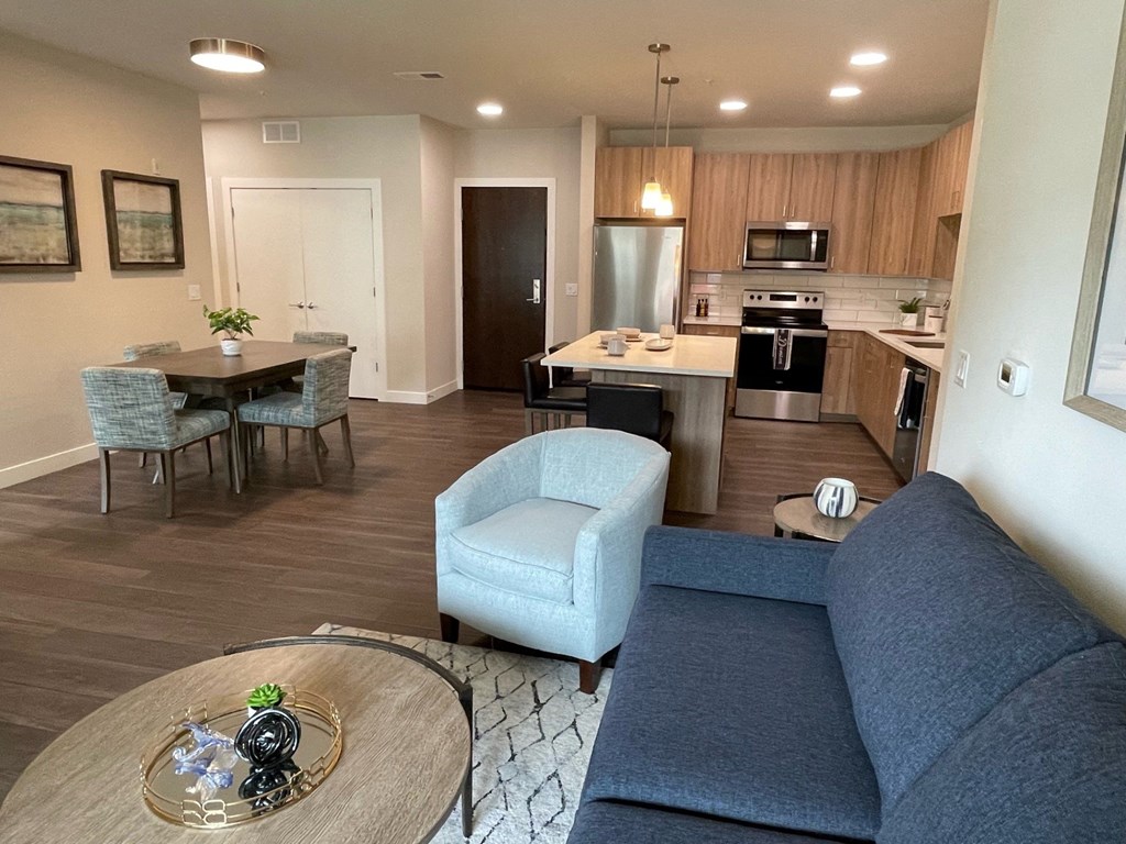 a living room with a couch a table and a chair and a kitchen with a stove and