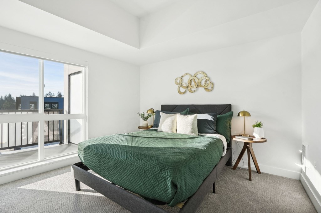 A bedroom with a large bed and a balcony with a view of buildings outside at AVIVA Apartments in Gresham Oregon