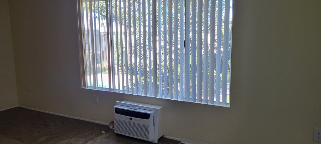 Living room with air conditioner, hardwood flooring, and large window at IKARIA Apartments in Santee, California.