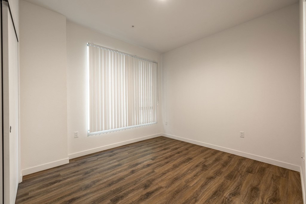 a bedroom with white walls and wood flooring and a window