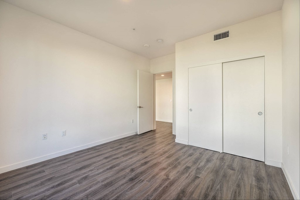 a bedroom with white walls and wood flooring and a closet