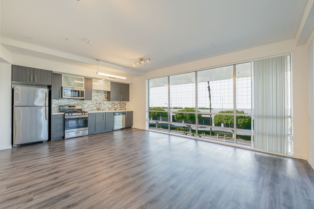 an empty living room with a kitchen and a large window