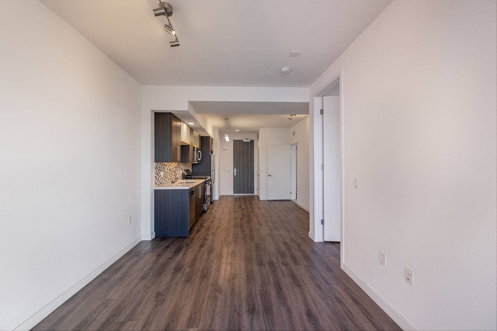 a living room and kitchen with white walls and wood flooring
