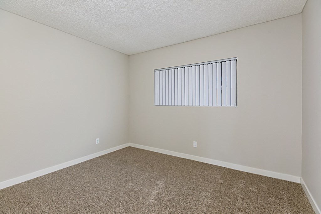 Carpeted bedroom with large window at Solara Apartments in Fallbrook, CA.
